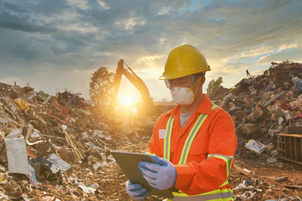 Waste management expert in a hard hat reviewing a tablet at a landfill