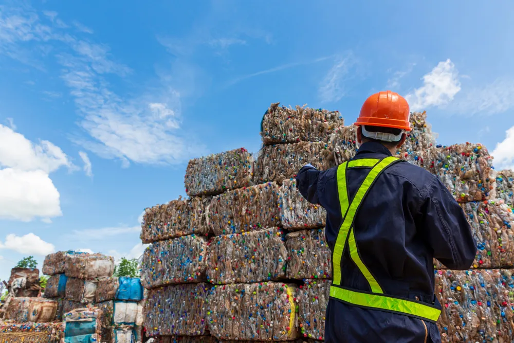 Worker in safety gear planning beside stacked recycling bales